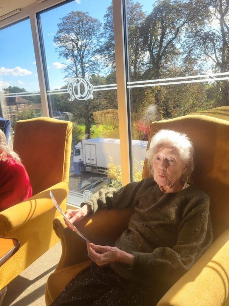 female resident wearing a green jumper sat in an armchair holding photo in her hand and reminiscing
