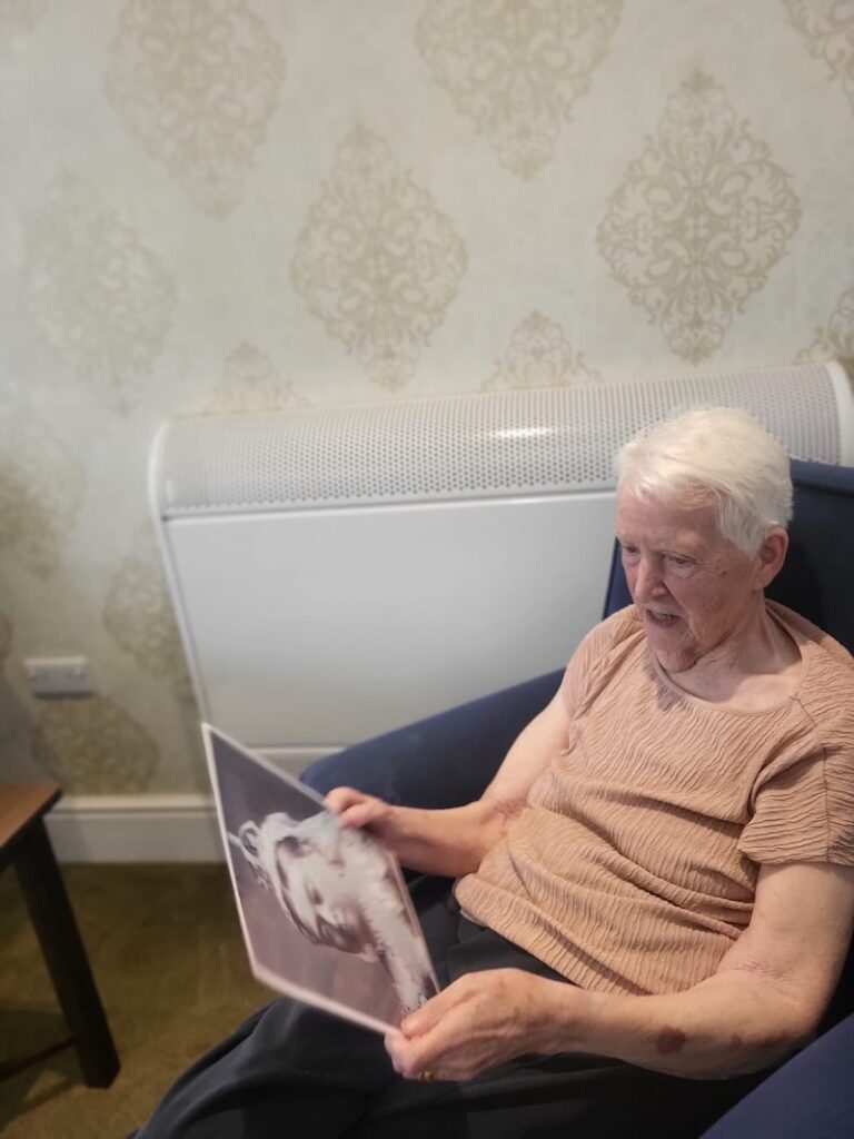 female resident wearing a pink top sat in an armchair holding photo in her hand and reminiscing