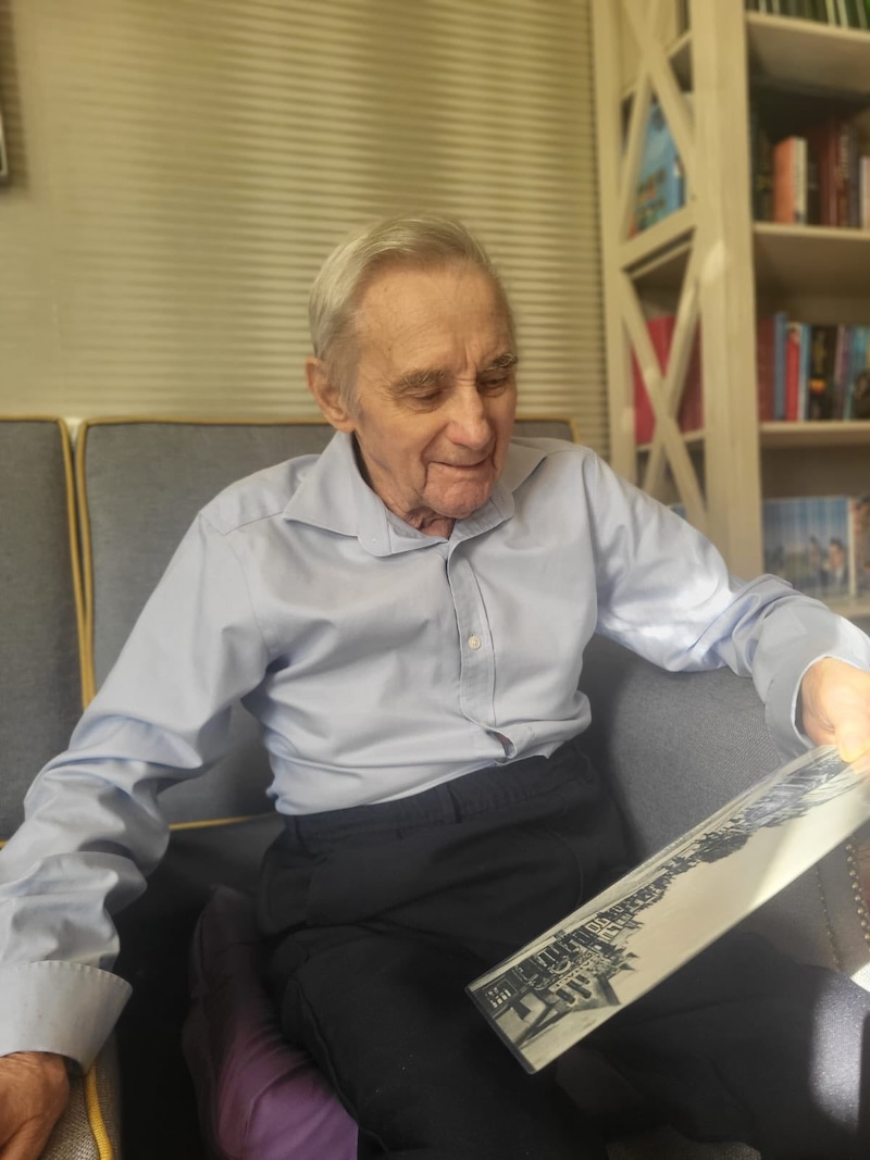 male resident wearing a blue shirt sat in an armchair holding photo in his hand and reminiscing