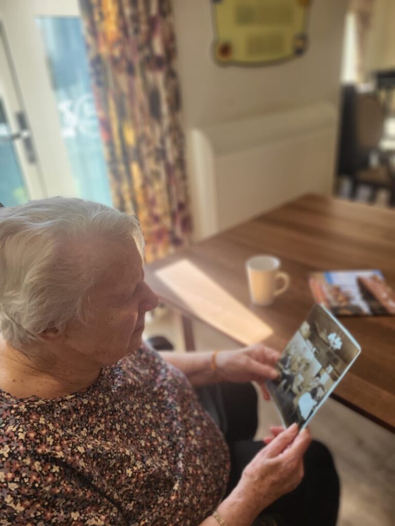 female resident wearing a flowery top sat in an armchair holding photo in her hand and reminiscing