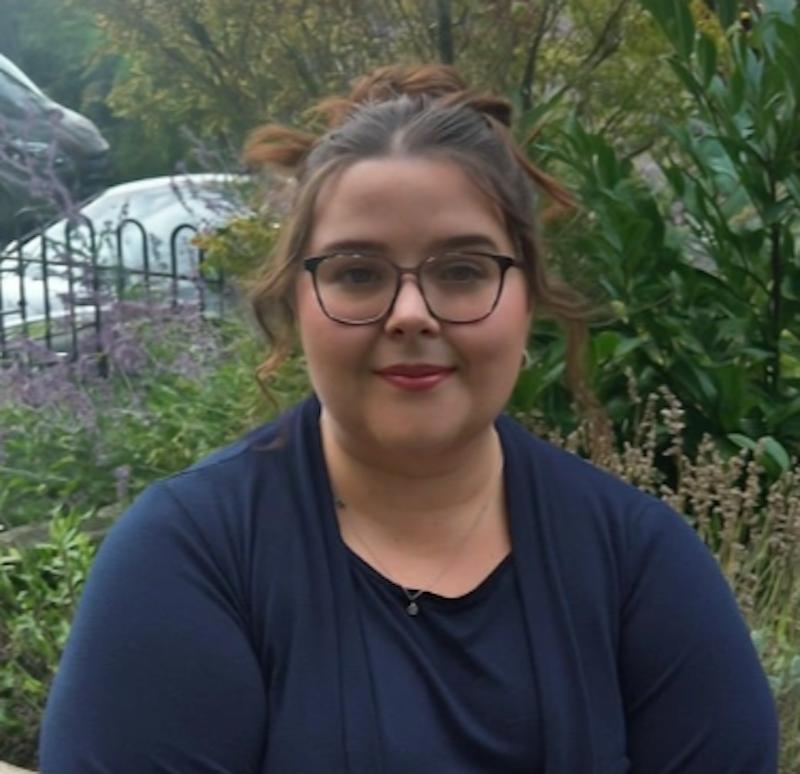 Lady with brown hair tied up in a blue top having a headshot taken for the team page