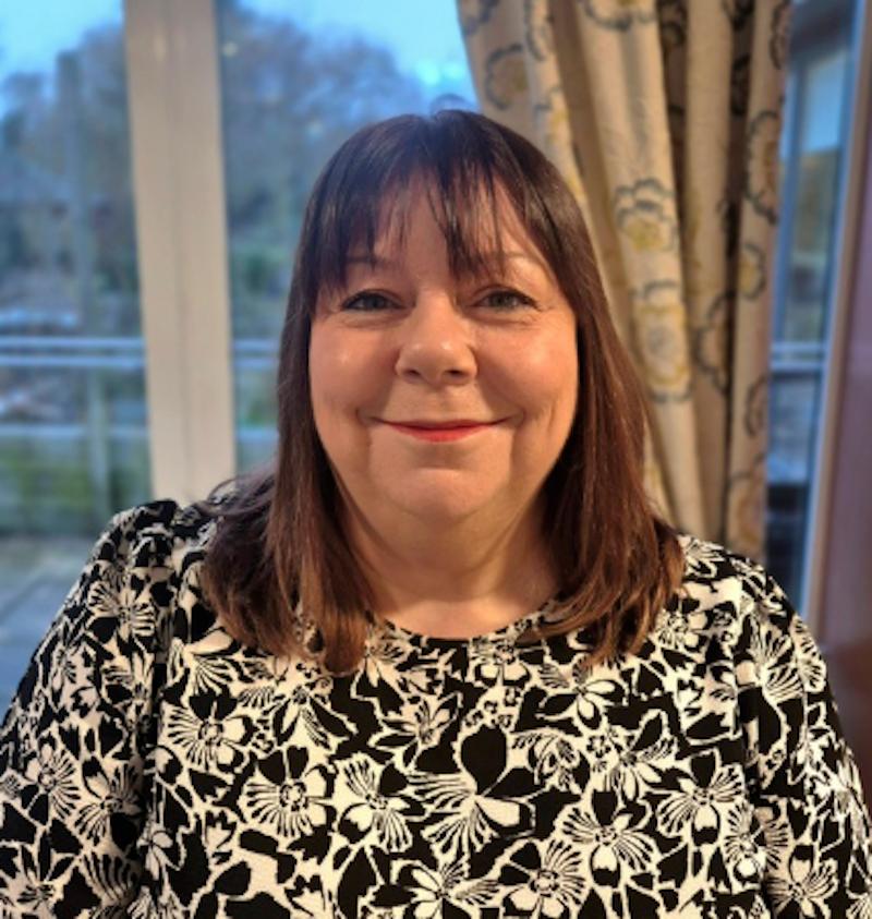 Lady with brown hair in a in a black and white flower patterned top having a headshot taken for the team page