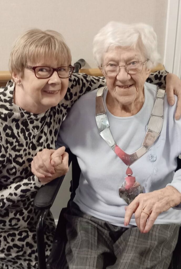family member sat with her arm around an elderly lady smiling