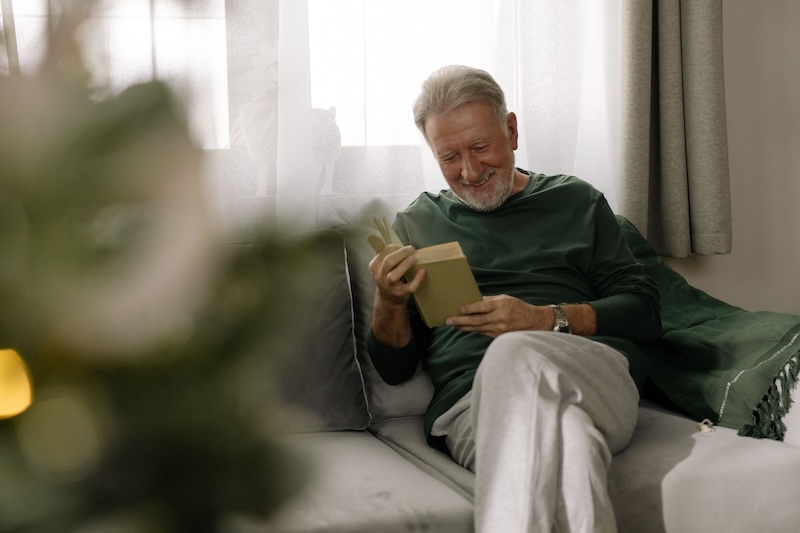 older man reading a book next to christmas tree