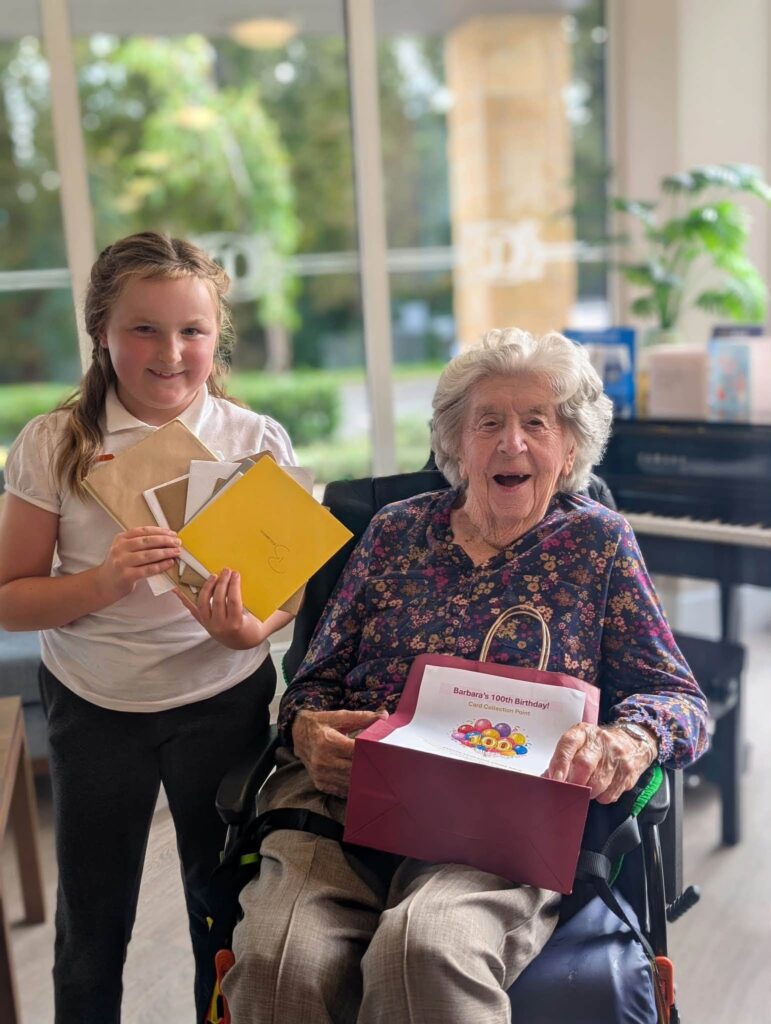older lady in a wheelchair with a girl standing next to. her holding some cards